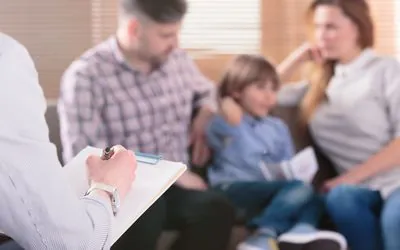 Parents et leur fils en rencontre avec un professionnel qui prend des notes pendant une consultation familiale