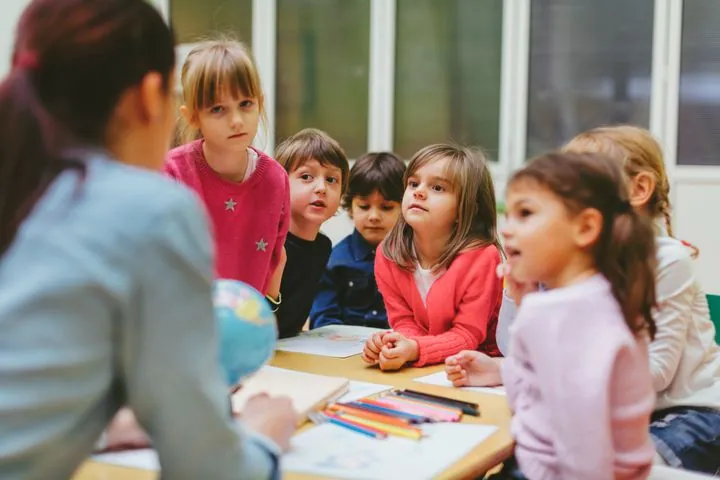 Enseignante qui anime un petit groupe de filles et de garçons autour d'une table en classe