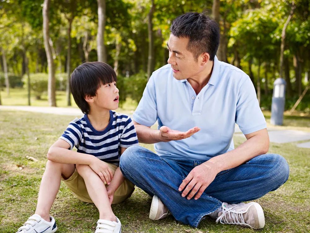 Un parent assis dans l'herbe qui discute calmement avec son fils