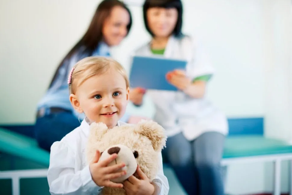 Jeune enfant qui tient un ourson en peluche pendant une évaluation avec deux professionnelles