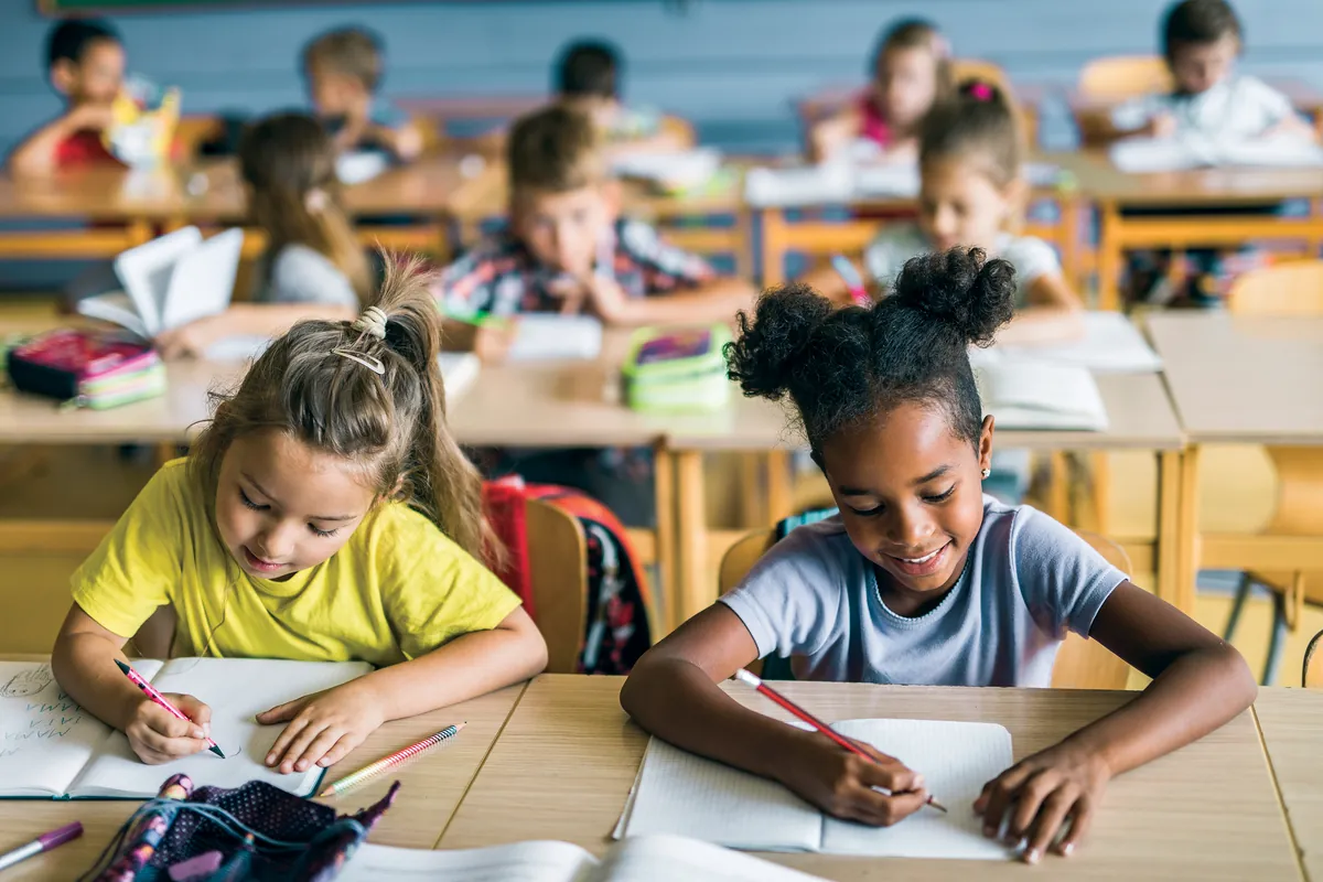 Élèves du primaire qui écrivent à leur pupitre dans une classe animée