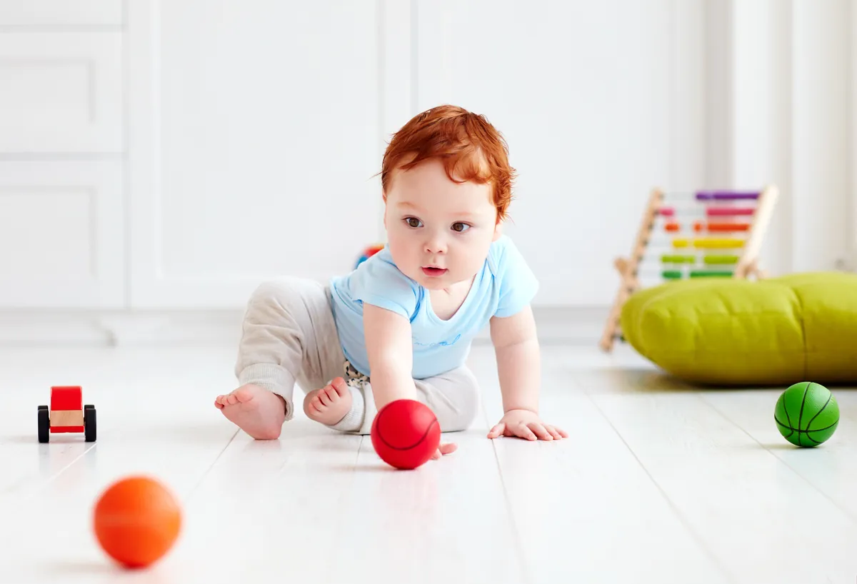 Bébé à quatre pattes qui s'approche de balles sensorielles sur le plancher d'une salle de jeu lumineuse