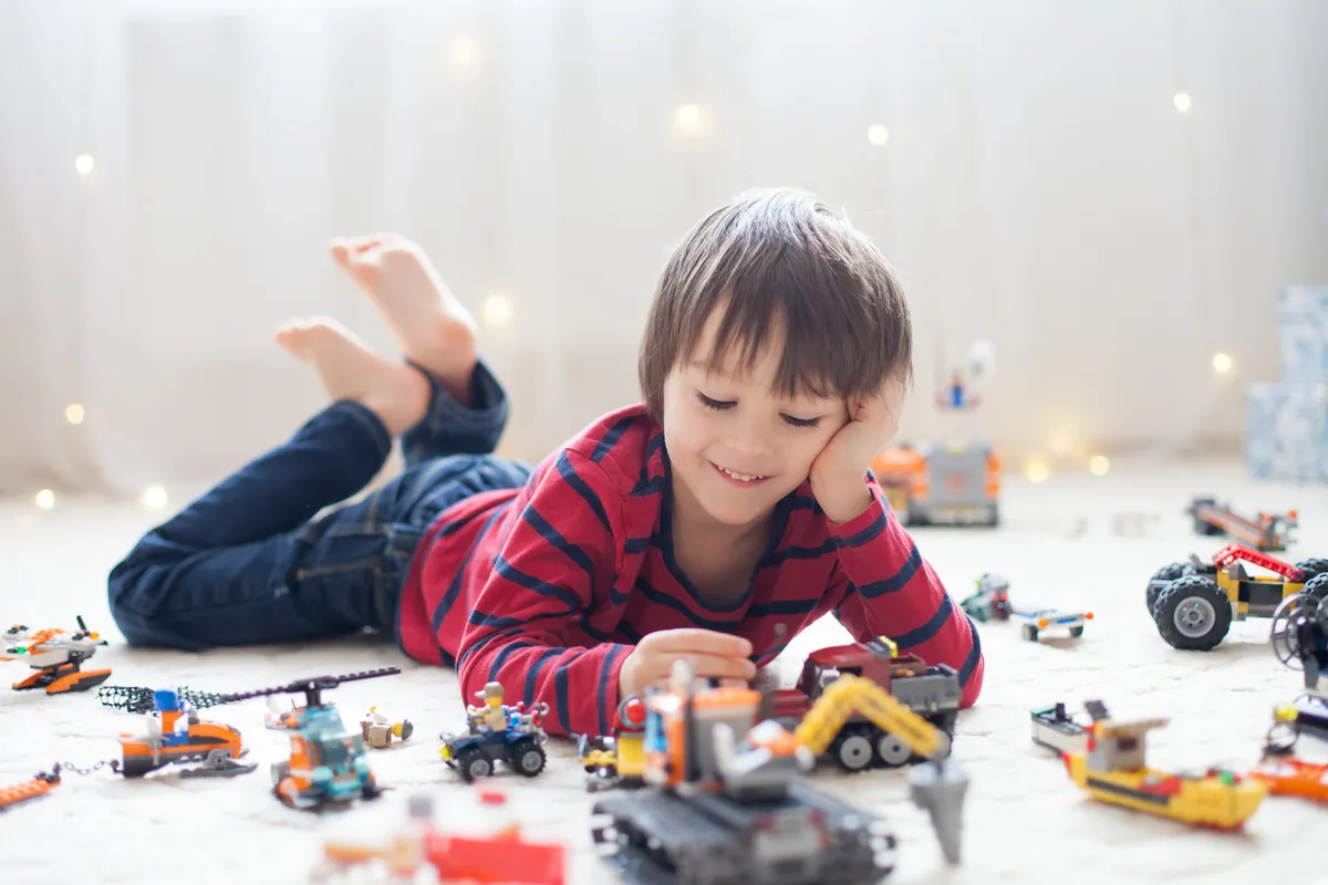 Garçon souriant allongé sur le plancher qui joue avec des véhicules de construction miniatures