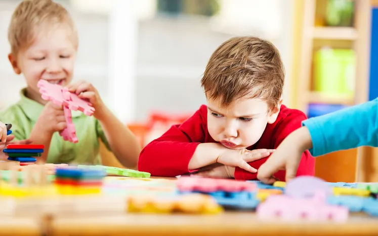 Deux garçons à une table de jeu, l'un frustré et l'autre calme — le jeu sensoriel aide l'enfant à gérer ses émotions
