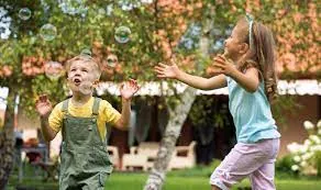 Deux enfants qui pourchassent des bulles de savon dans un jardin — stimulation visuelle et motrice