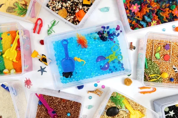 Vue de dessus de plusieurs bacs sensoriels remplis de riz coloré, de haricots, de jouets d'eau et de petites figurines