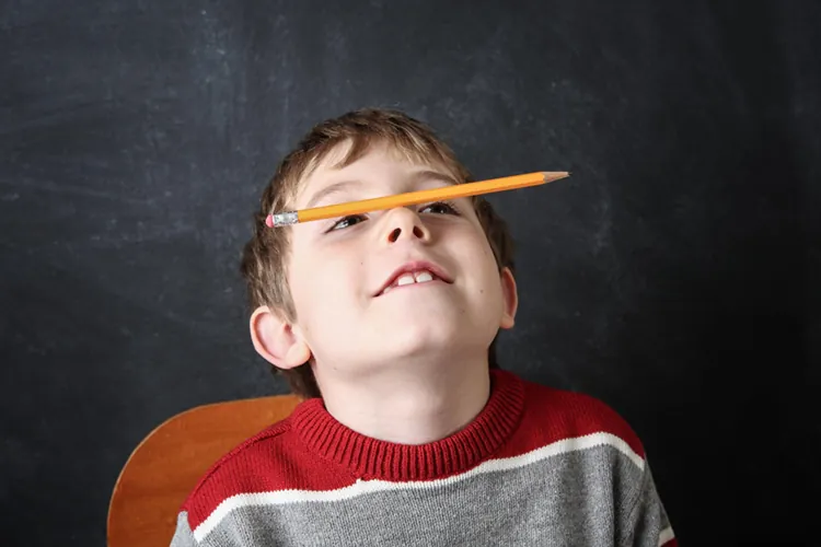 Écolier qui s'ennuie et tient un crayon en équilibre sur son nez devant un tableau noir