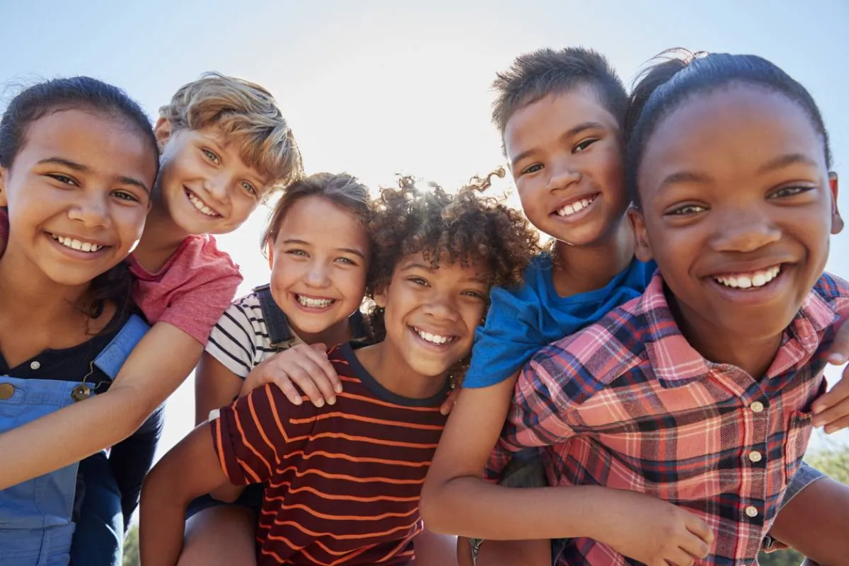 Groupe d'enfants souriants d'origines diverses qui posent ensemble à l'extérieur
