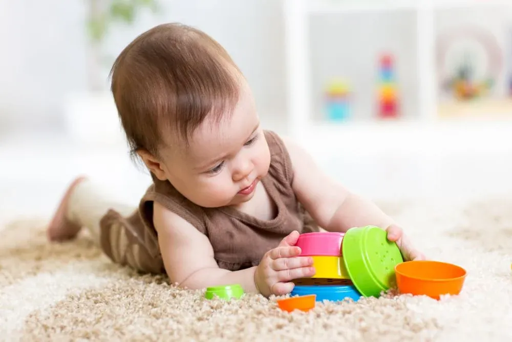 Bébé couché sur un tapis qui explore des gobelets à empiler colorés