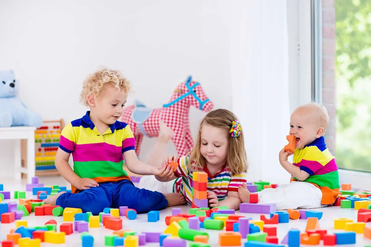 Trois jeunes enfants qui jouent librement avec des blocs de construction en mousse colorés dans une salle de jeu