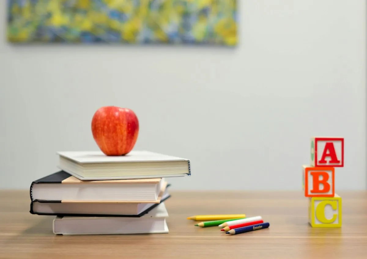 Pomme sur une pile de livres, avec crayons de couleur et blocs ABC, symboles des outils pédagogiques en classe