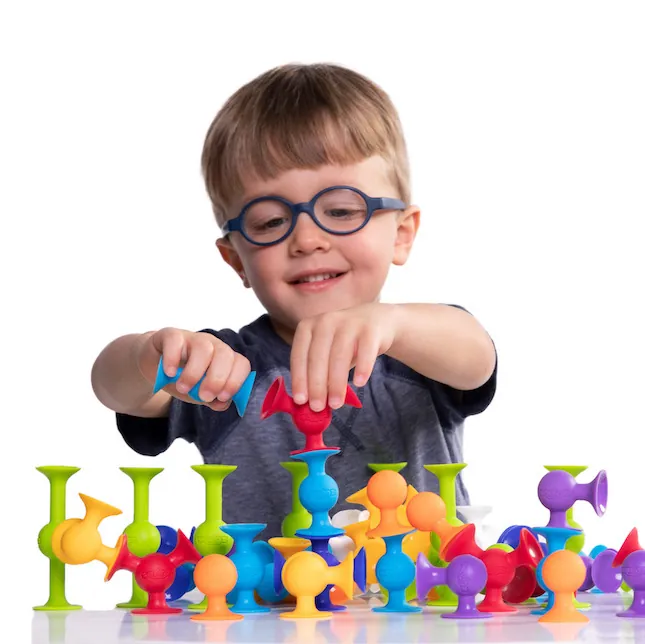 Jeune garçon à lunettes qui construit avec des jouets à ventouses colorés