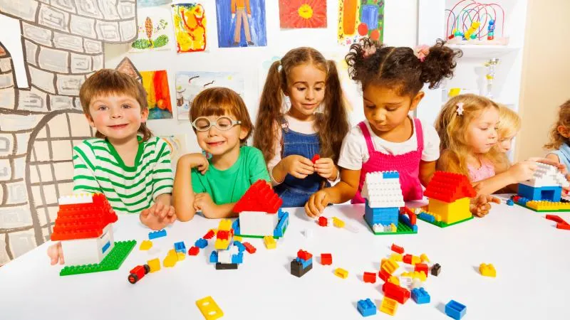 Enfants de maternelle souriants qui construisent des maisons en blocs colorés sur une table de classe