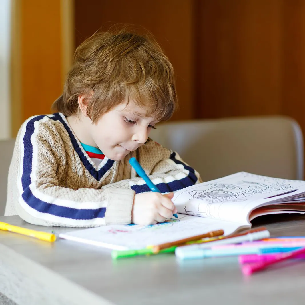 Jeune garçon concentré qui écrit et colorie dans un cahier à la table