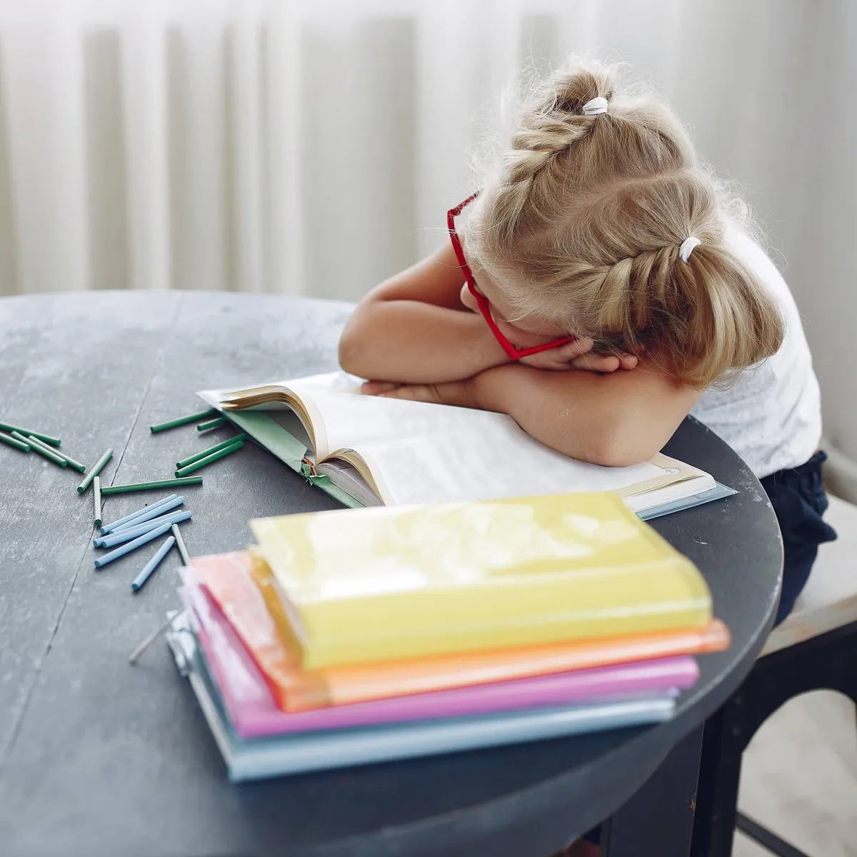 Fillette qui s'ennuie, sous-stimulée, la tête posée sur ses livres à son bureau