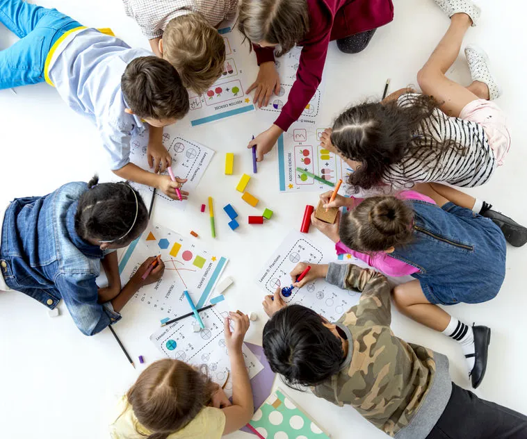 Groupe d'enfants couchés au sol qui dessinent et construisent avec des blocs lors d'une activité d'apprentissage concrète