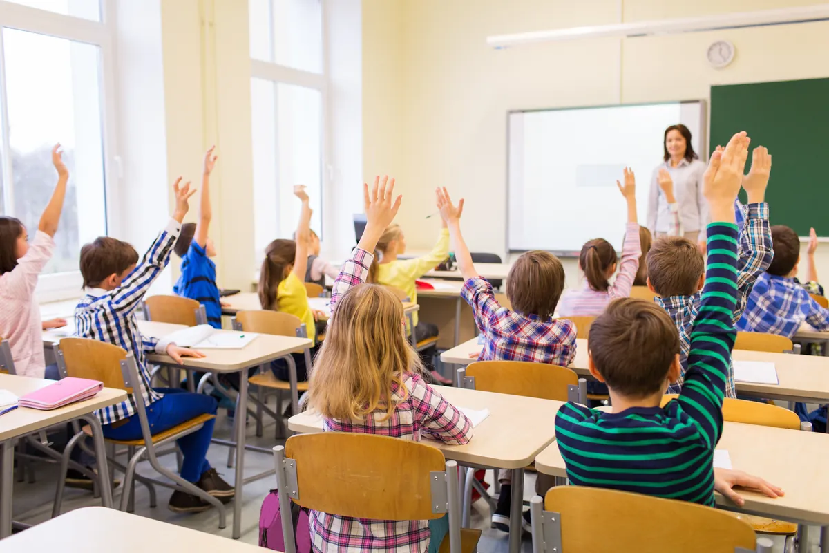 Élèves attentifs qui lèvent la main dans une classe du primaire