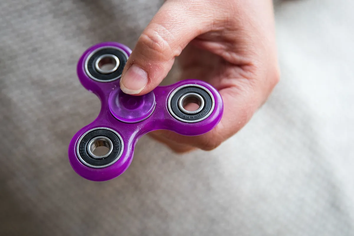 Main qui fait tourner un fidget spinner violet, un fidget rotatif qui apaise et soutient la concentration