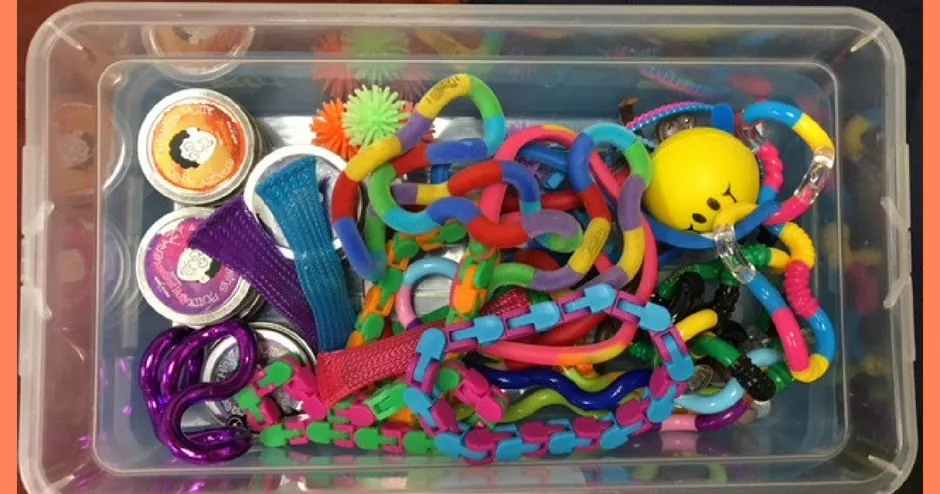 Bac transparent rempli de fidgets variés, comme une boîte sensorielle partagée en classe