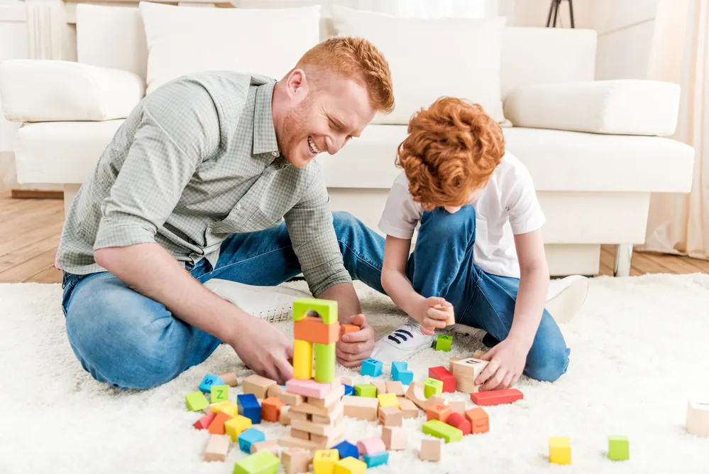 Un père et son fils assis au sol qui construisent avec des blocs de bois — du jeu libre à la maison