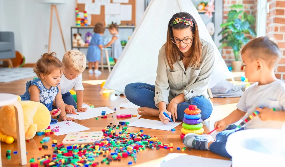 Classe Montessori avec tables basses où les enfants travaillent de façon autonome sous l'œil de l'enseignante