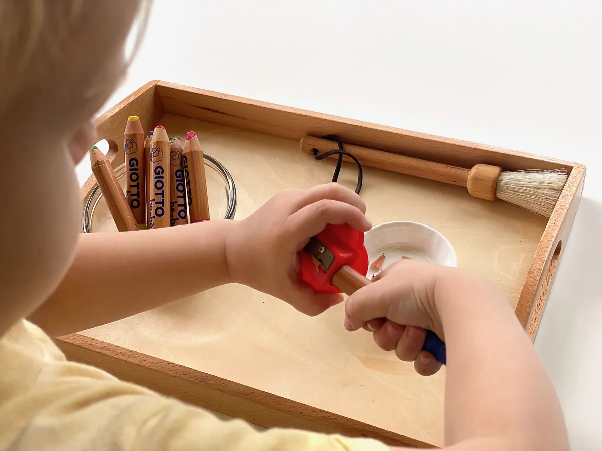 Enfant qui utilise un plateau de vie pratique en bois avec des crayons et un petit pinceau — une activité Montessori classique