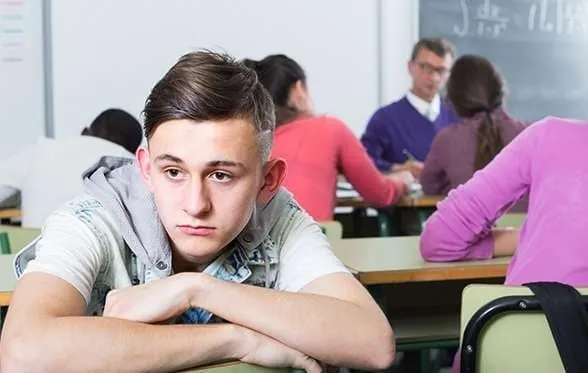 Adolescent autiste à l'air replié et isolé à son pupitre en classe