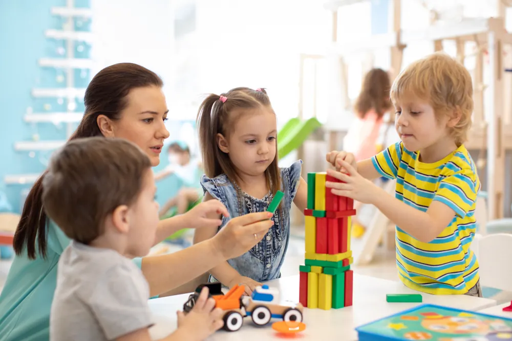 Parent qui empile patiemment des blocs colorés avec de jeunes enfants à une table de jeu