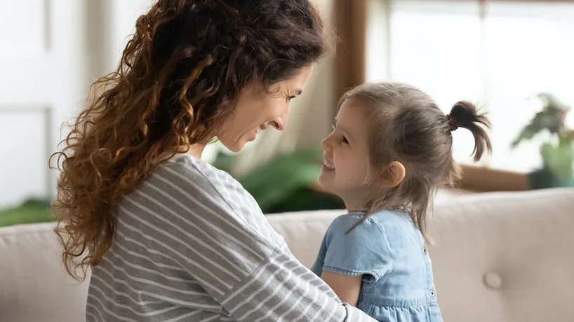 Mère penchée qui sourit à sa jeune fille dans le salon