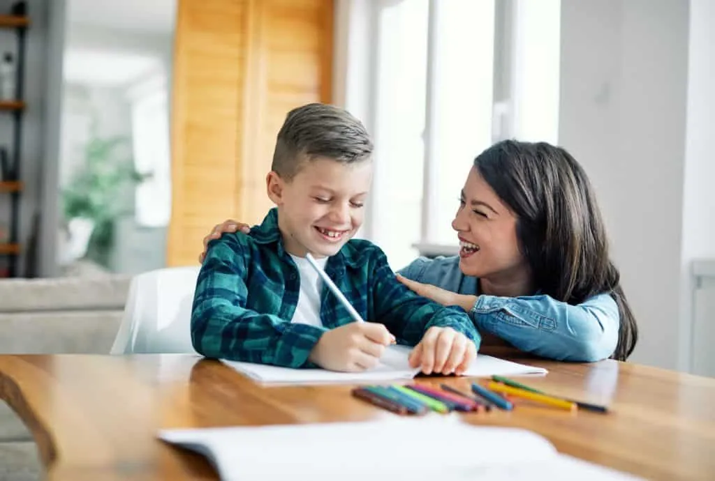 Mère souriante qui encourage son fils pendant qu'il dessine à la table, pour renforcer son estime de soi