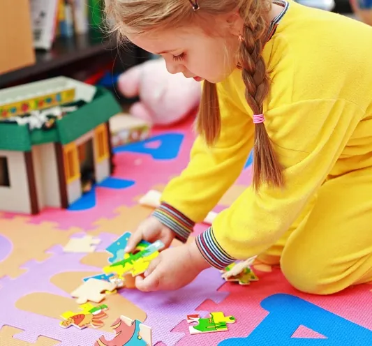 Fillette qui assemble un casse-tête coloré sur un tapis de mousse