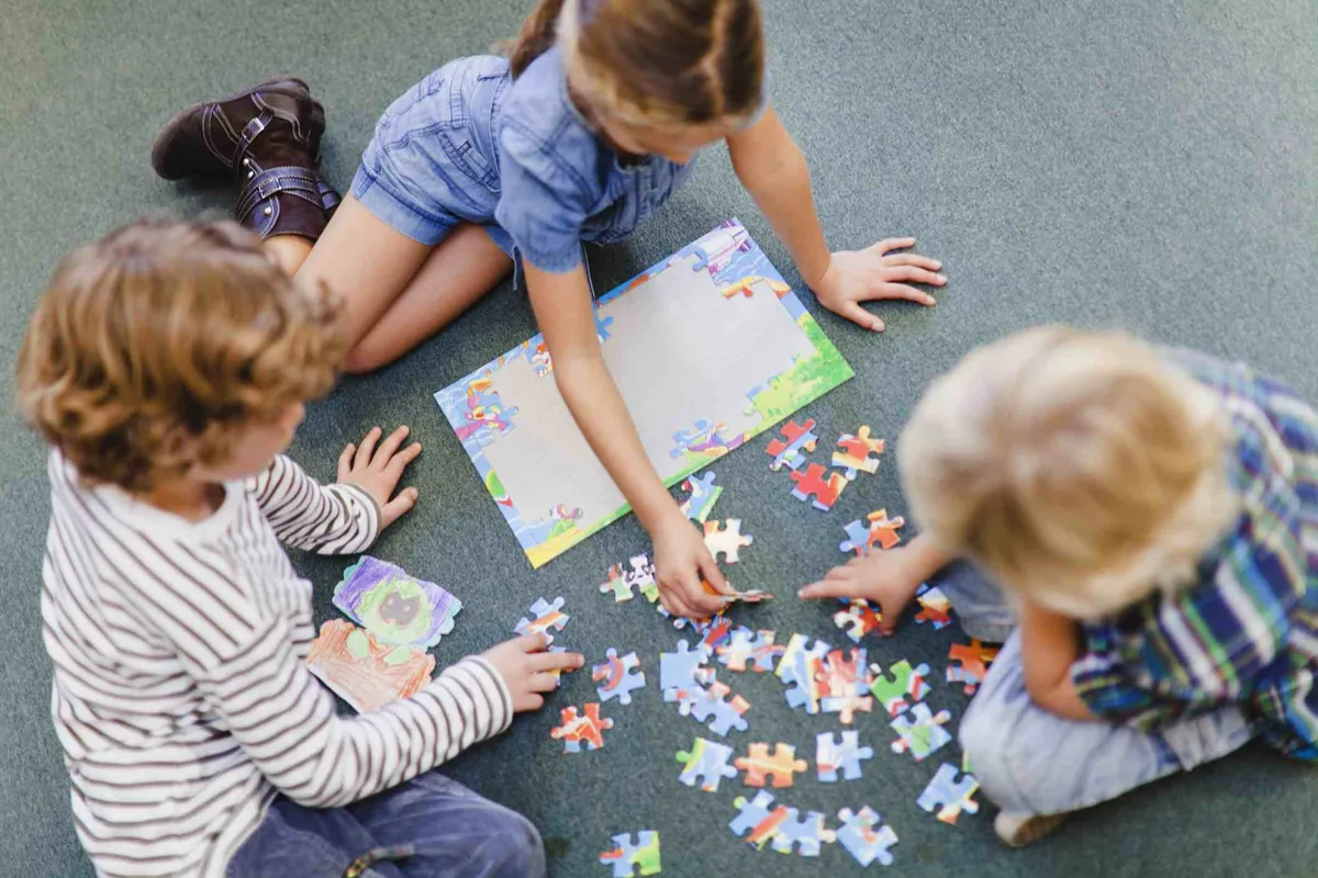 Trois enfants assis par terre qui assemblent un casse-tête ensemble