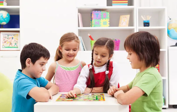 Quatre enfants qui jouent ensemble à un jeu de société à une table, en apprenant à attendre leur tour