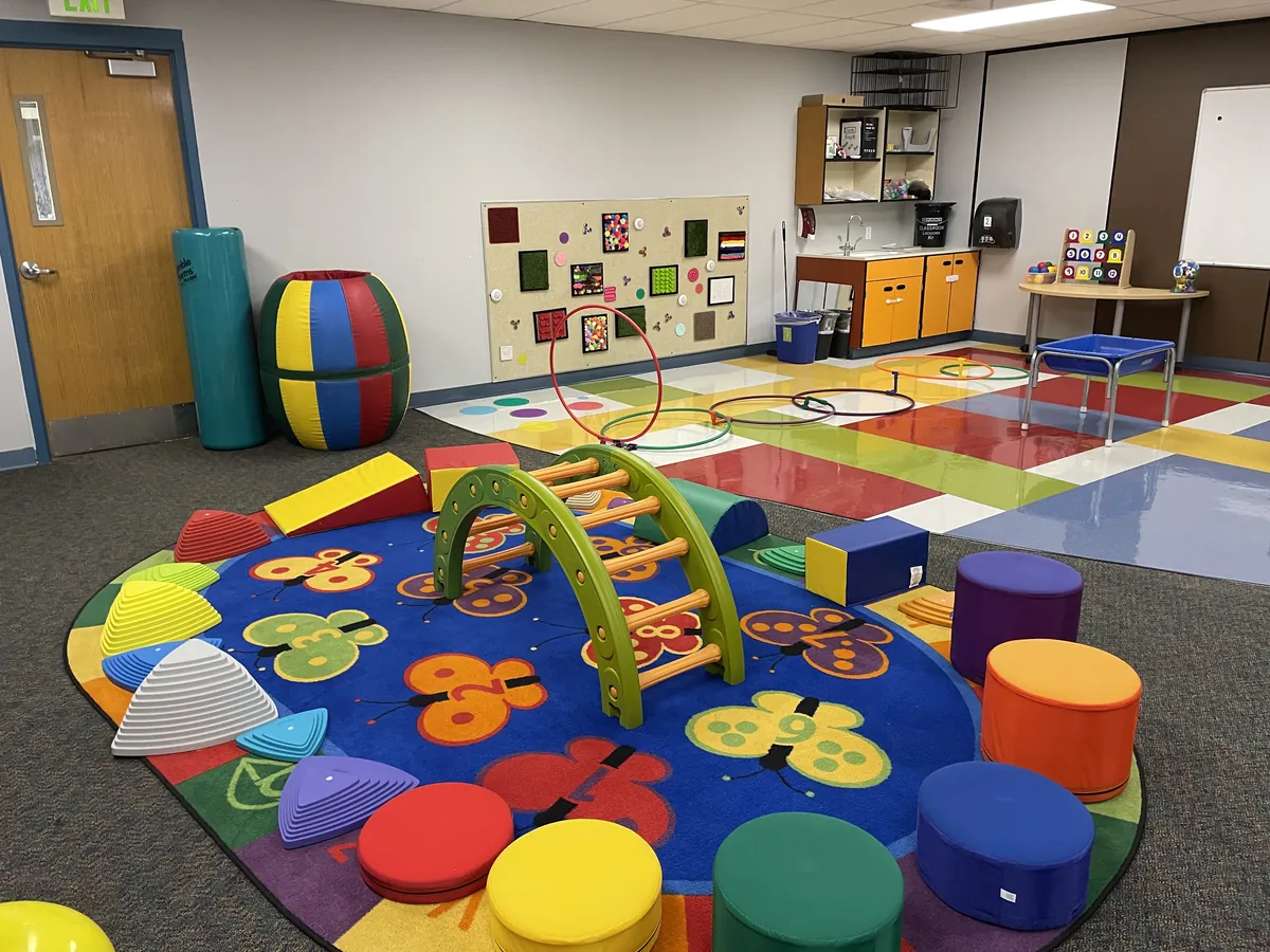 Salle sensorielle d'école avec tapis mous, arche d'escalade et coussins de sol colorés