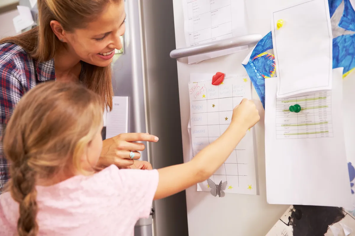 Mère et fille qui consultent ensemble un tableau de progrès sur le frigo