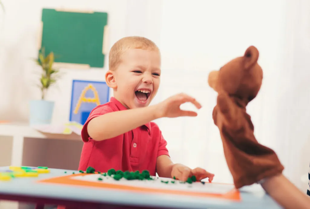 Garçon qui rit en jouant avec une marionnette, pendant une pause sensorielle ludique