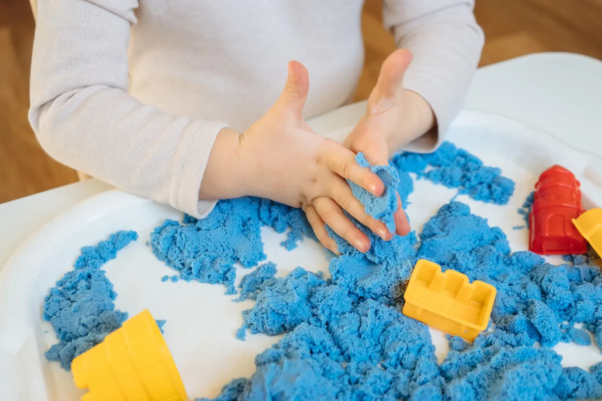 Mains d'enfant qui pétrissent du sable cinétique bleu avec des moules, une activité sensorielle tactile