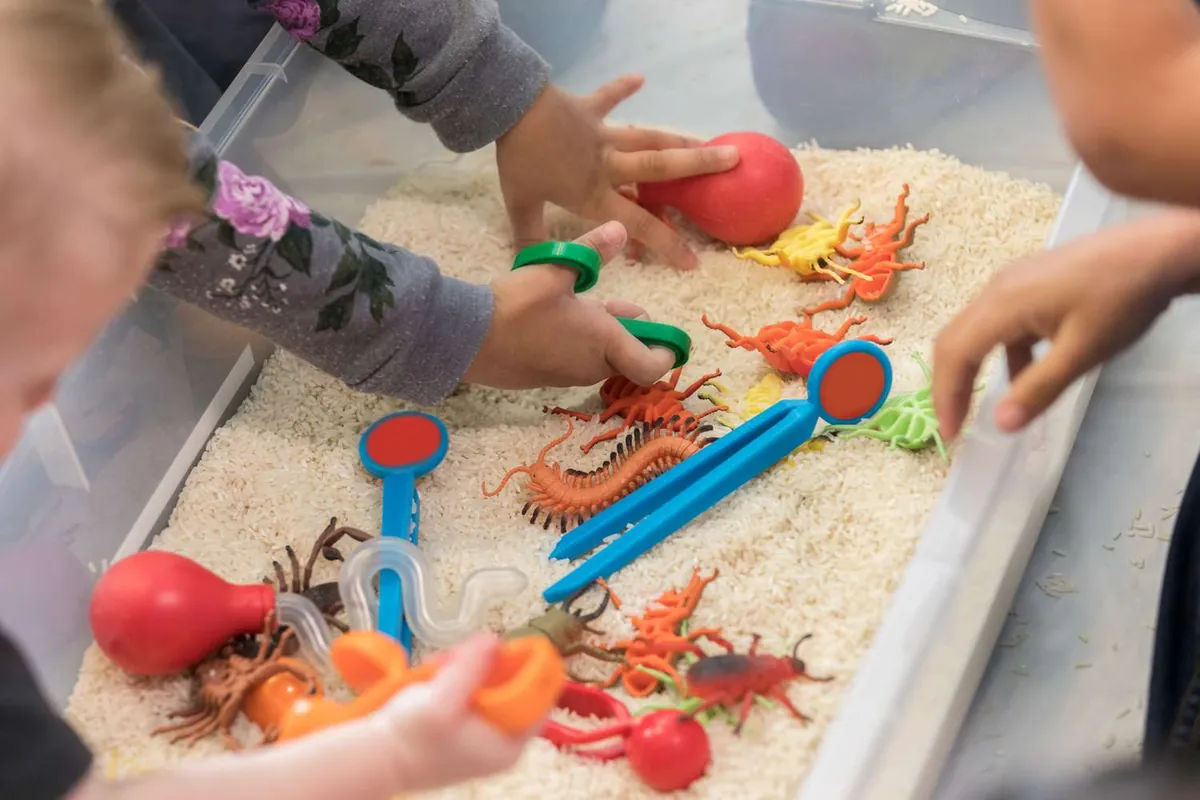 Mains d'enfants explorant un bac sensoriel de riz avec des pelles et des insectes jouets