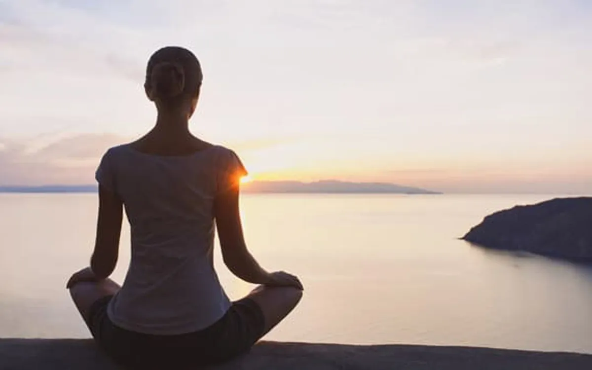 Personne qui médite en tailleur au bord de la mer au coucher du soleil, une pratique simple de pleine conscience