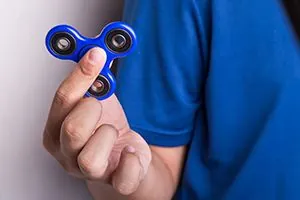 Main qui fait tourner un fidget spinner bleu, un fidget simple contre l'anxiété