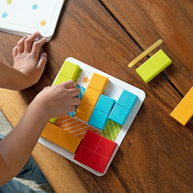 Enfant qui résout un casse-tête logique en blocs de bois colorés sur un plateau