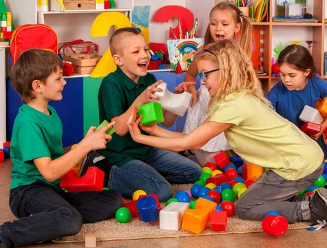 Élèves qui rient et jouent ensemble avec des blocs et des balles sur le plancher de la classe