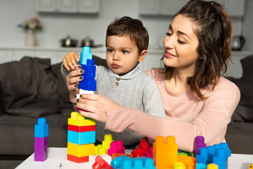 Une mère supervise son jeune fils qui empile des blocs de construction colorés