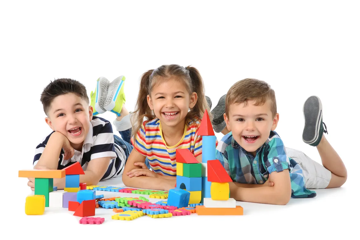 Trois enfants souriants allongés au sol près d'une pile de blocs de construction colorés