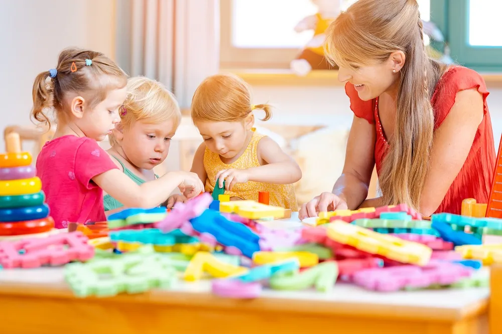 Une éducatrice et de jeunes enfants qui construisent ensemble avec des pièces de construction colorées