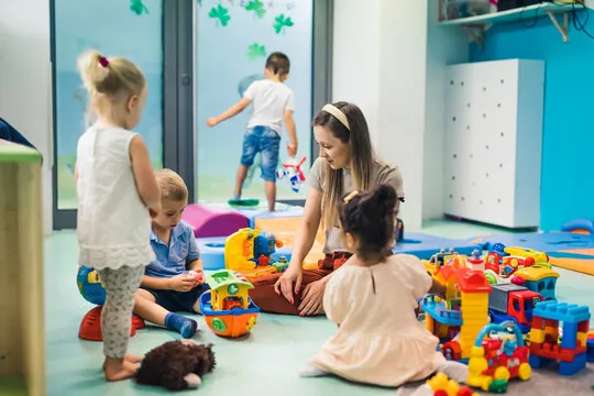 Une éducatrice assise au sol avec un petit groupe d'enfants qui jouent avec des jeux de construction