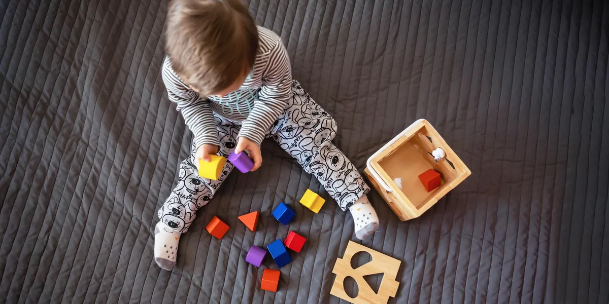 Tout-petit assis sur une couverture qui explore les blocs de bois colorés d'un trieur de formes