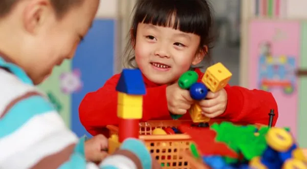 Fillette souriante qui joue avec des jouets de construction colorés à une table avec un ami