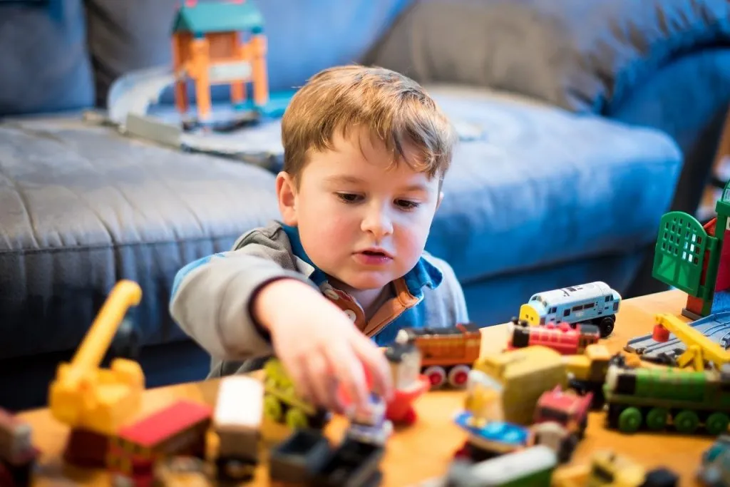 Jeune garçon absorbé par son jeu avec des véhicules et des pièces de construction sur une table