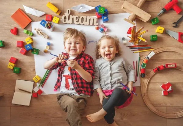 Deux enfants rieurs allongés au sol, entourés de jouets en bois, de blocs et de matériel de bricolage